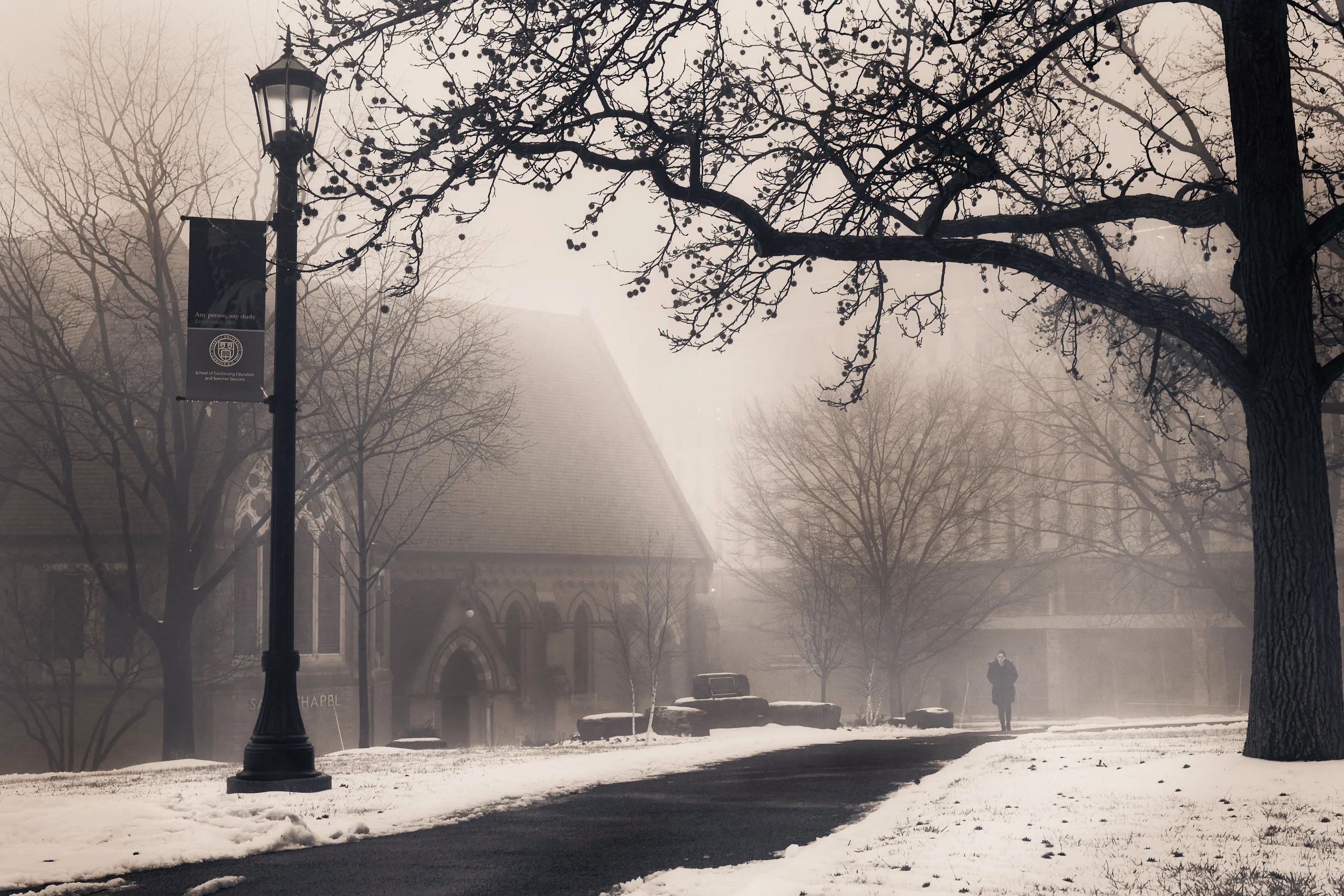 Brand & location — campus in winter fog, lamp post, figure walking in mist