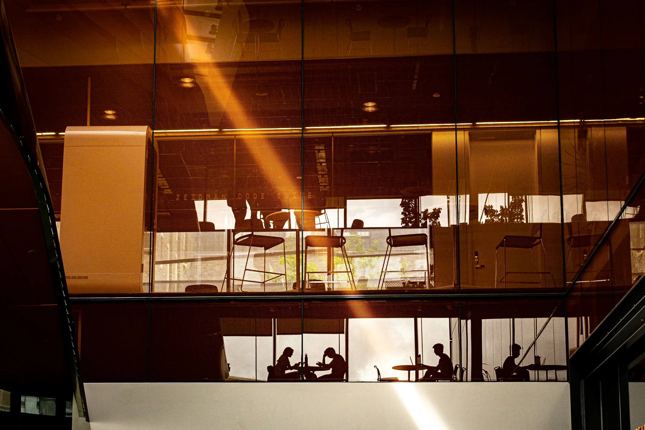 Brand & location — people silhouetted behind glass facade in golden hour light