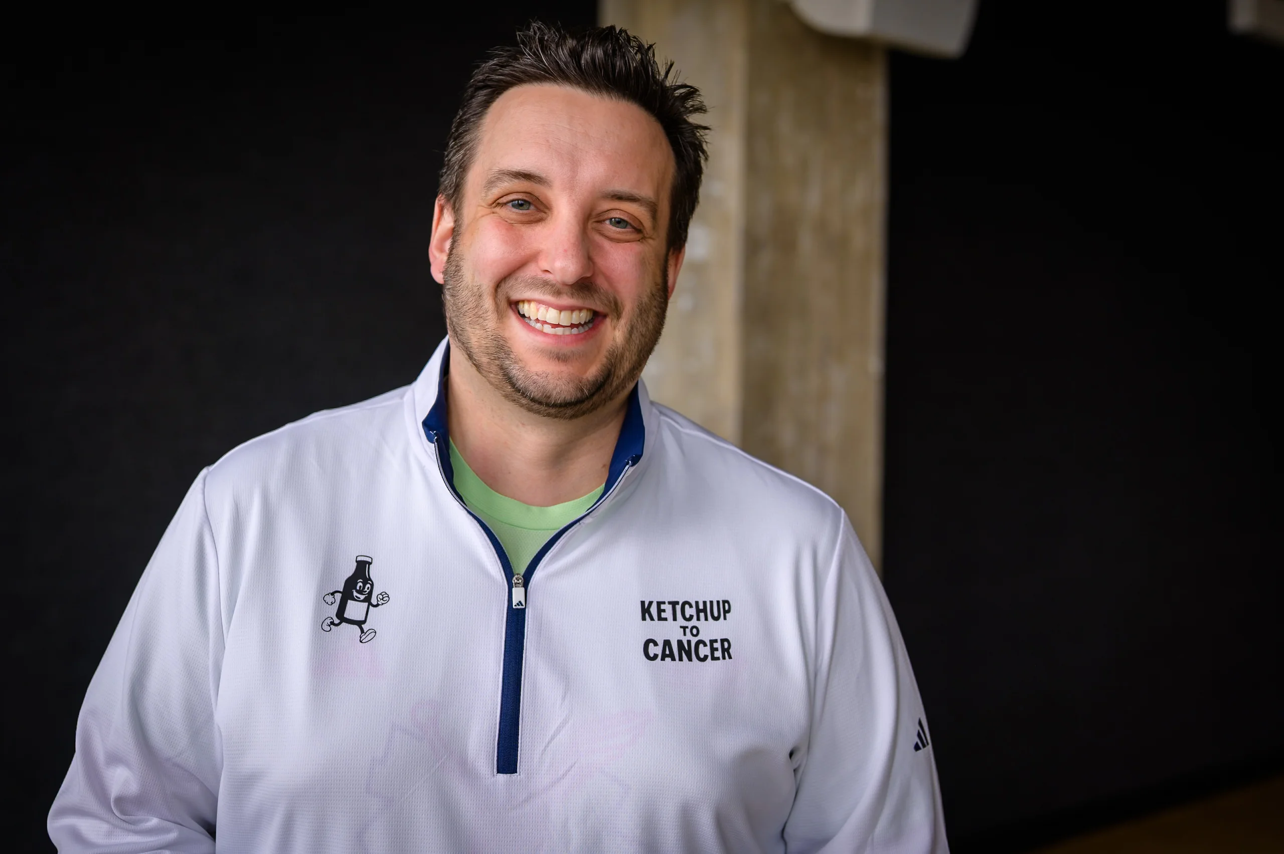 Brand & location — man in branded jacket, smiling, dark background