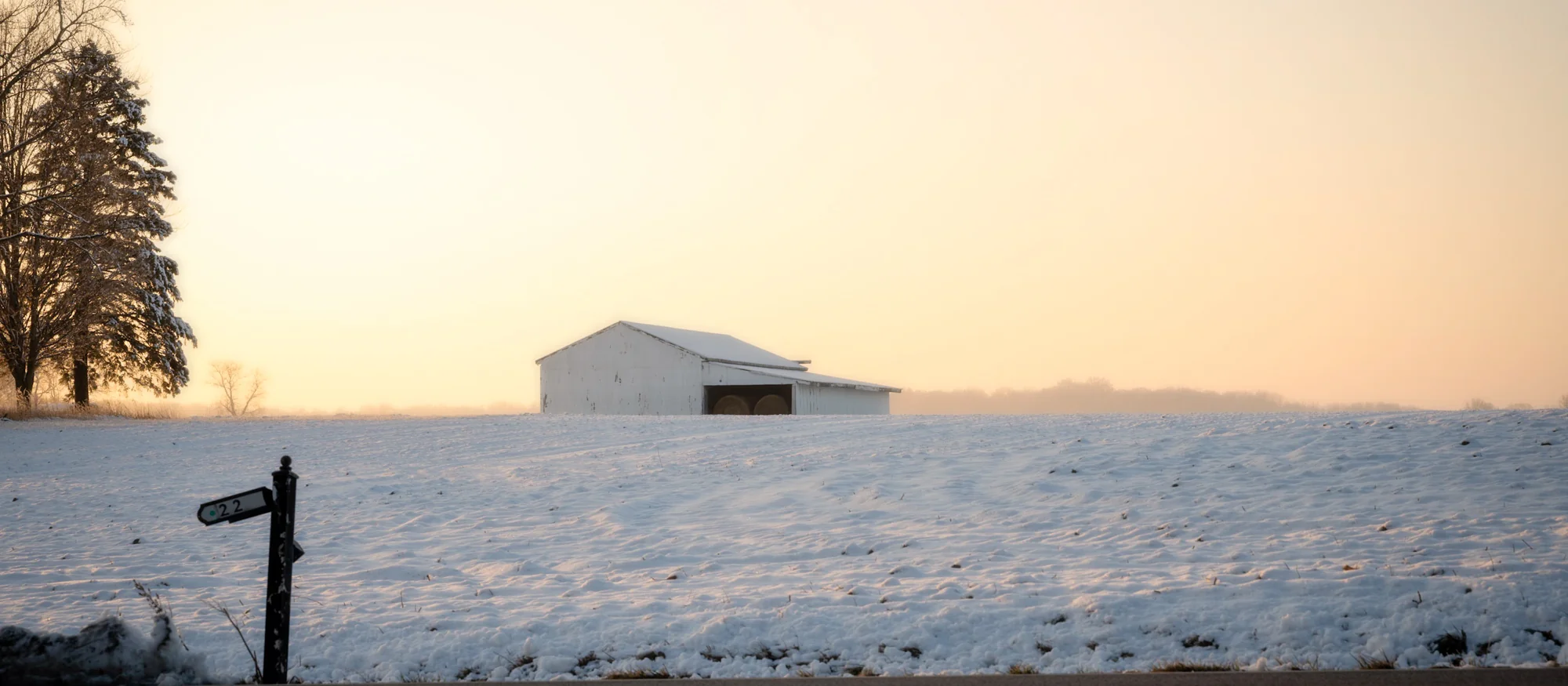 White barn in snow-covered field, golden mist at winter sunset