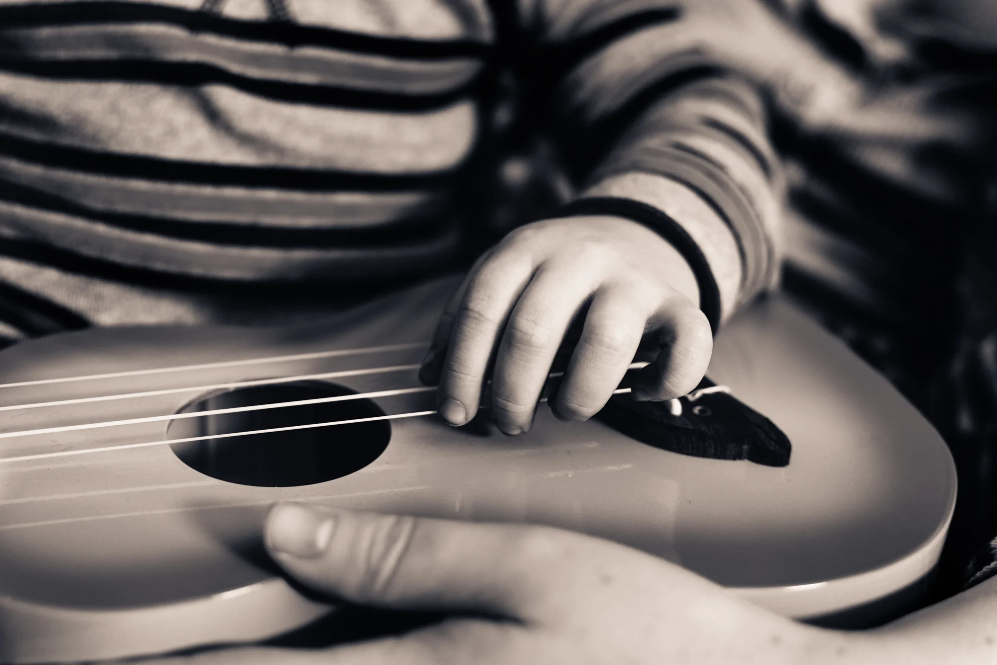 Portrait — child's hands on a ukulele, close crop