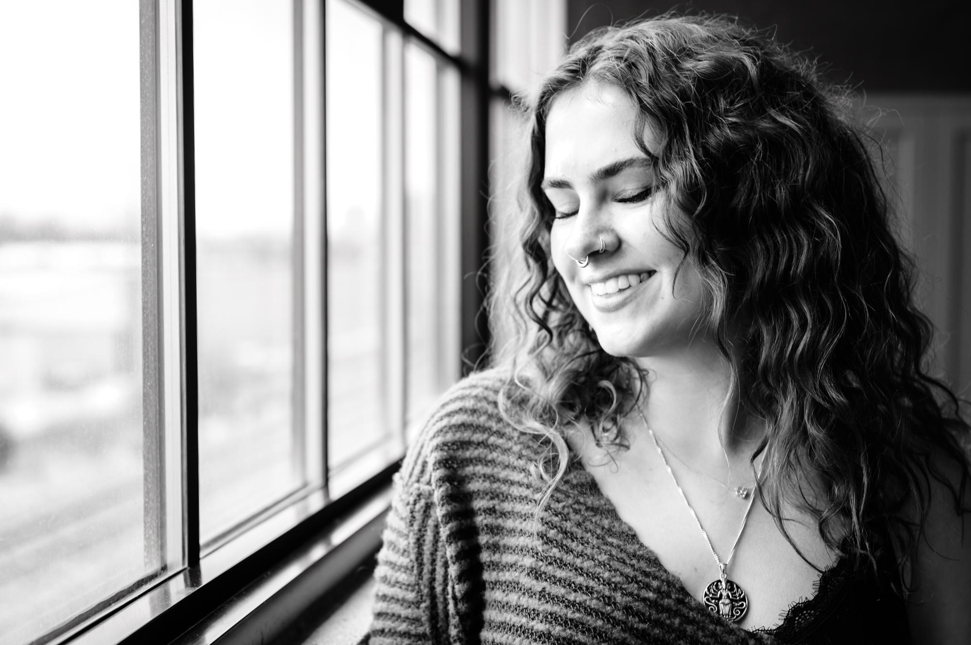 Portrait — woman with curly hair, eyes closed, smiling at window