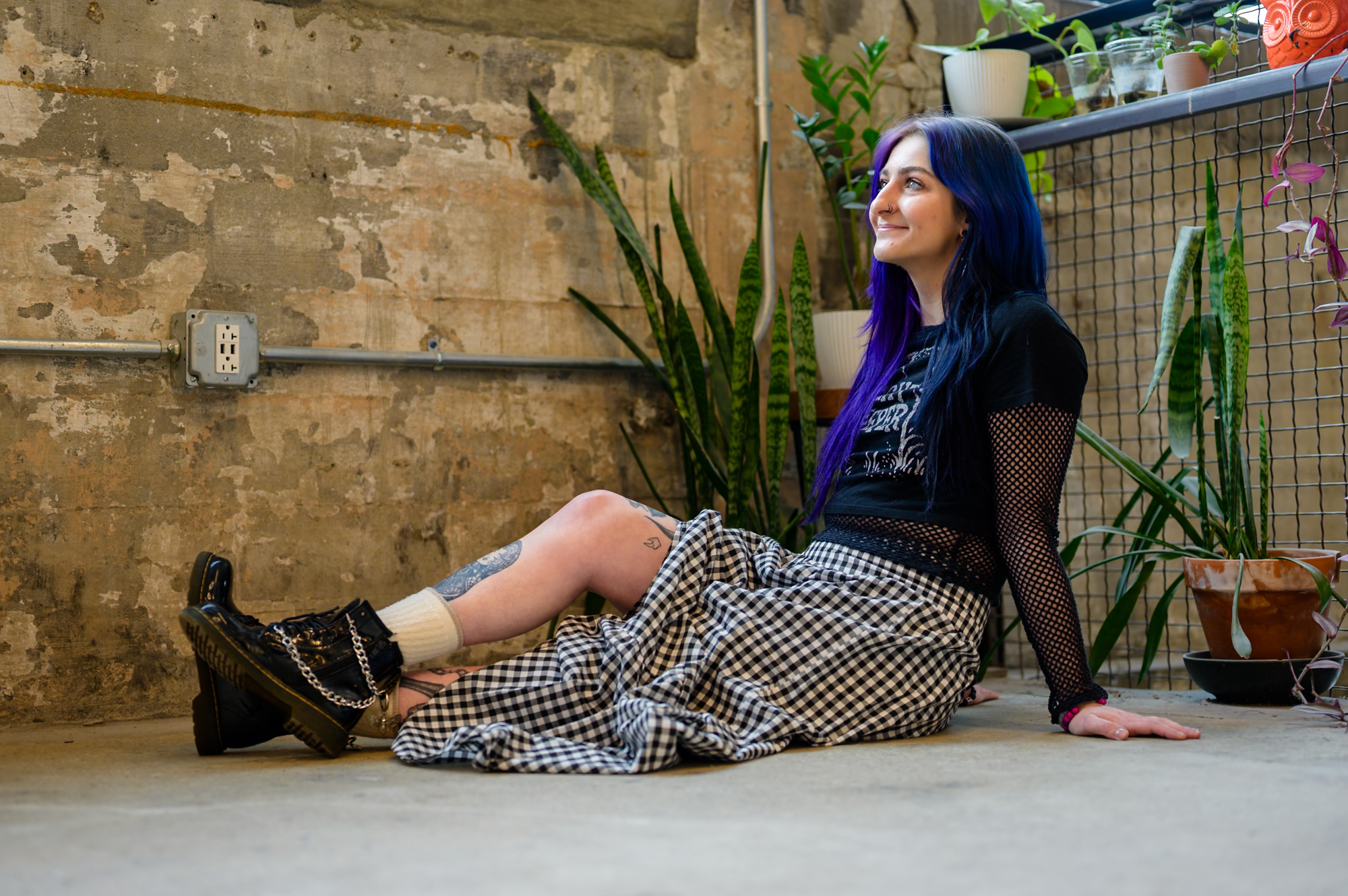 Portrait — woman with purple hair, seated against rough wall
