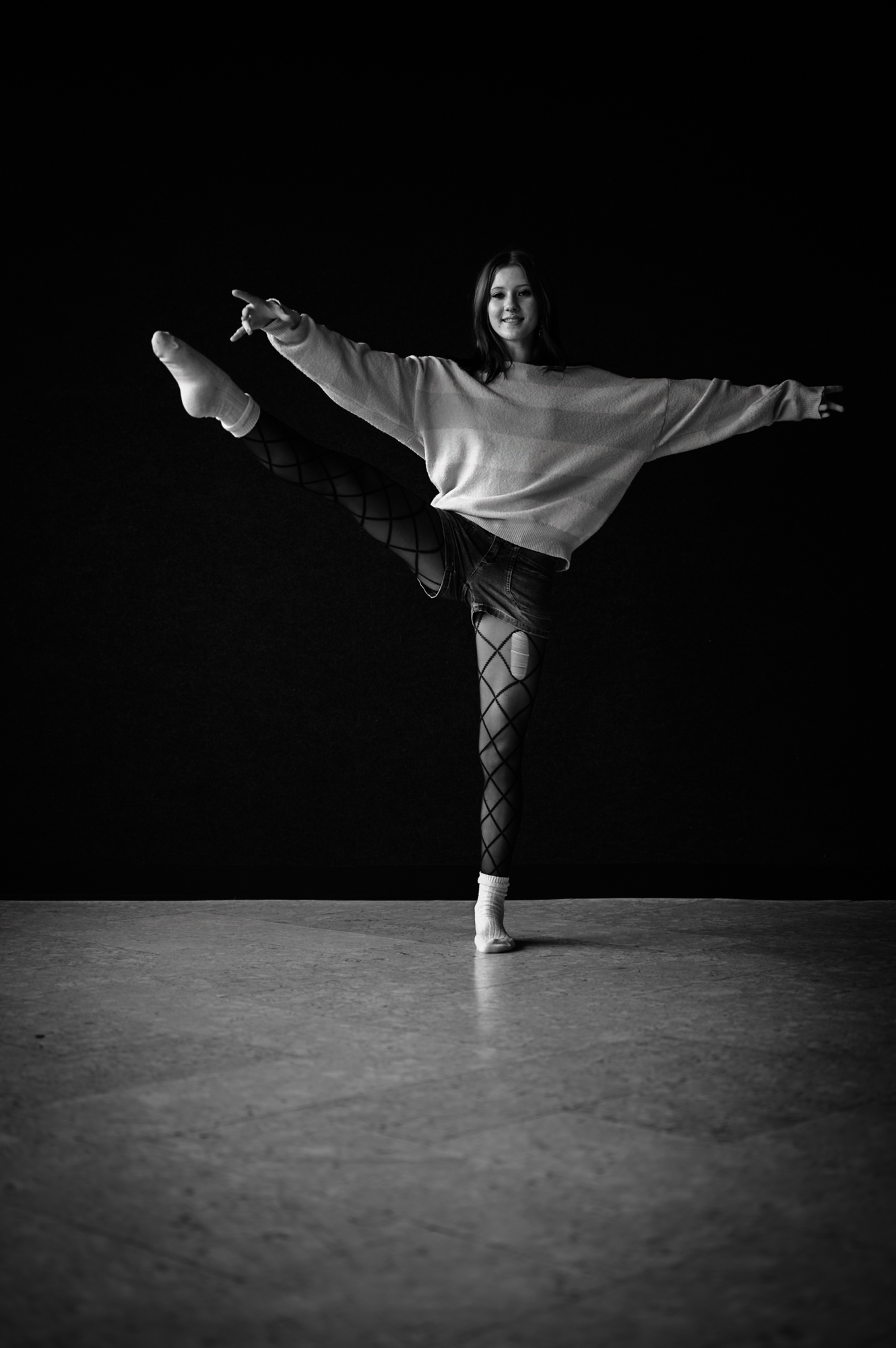 Portrait — dancer with arms wide and one leg raised, dark stage