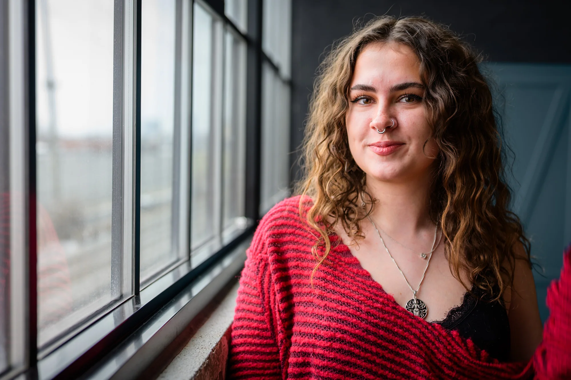 Portrait — woman smiling by a window, red sweater, warm natural light